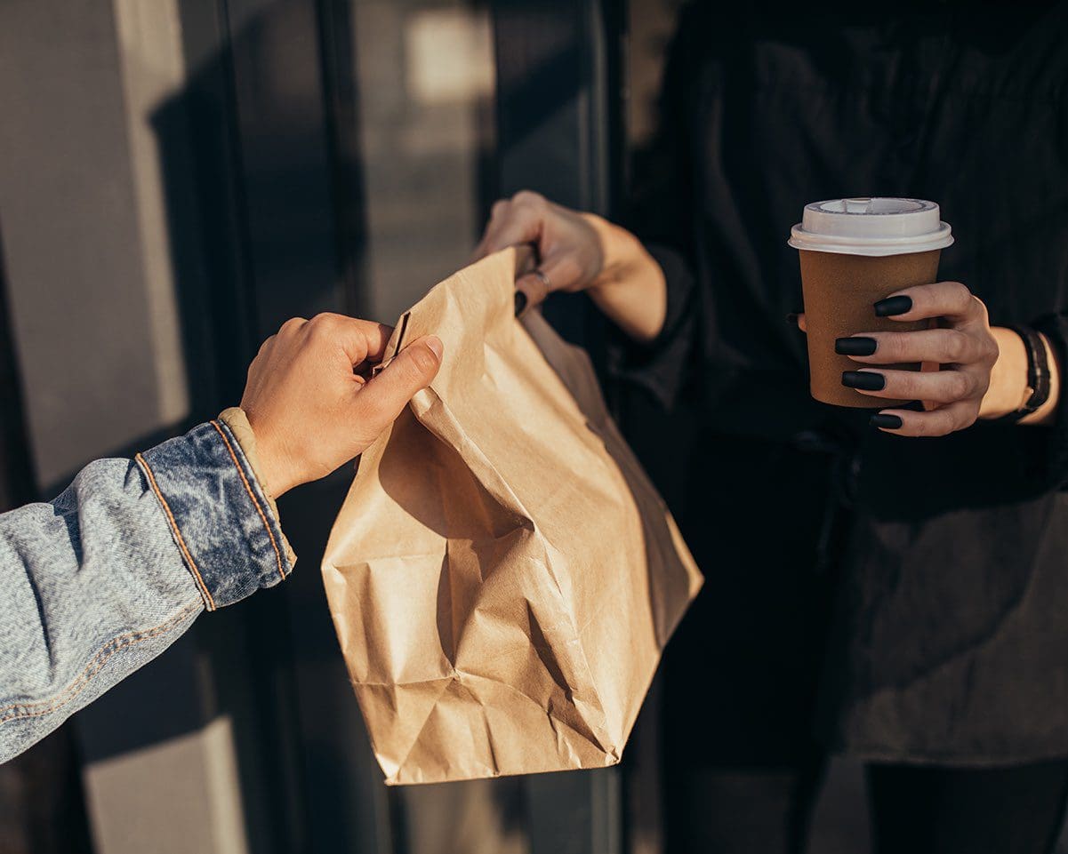 Woman taking takeaway paper bag with food and coffee to go