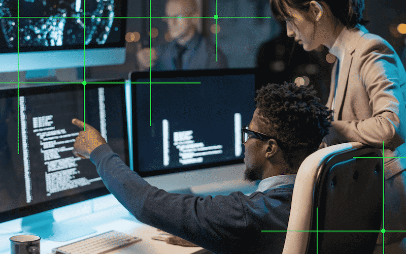 Businessman pointing at coded data on computer screen while explaining it to female colleague